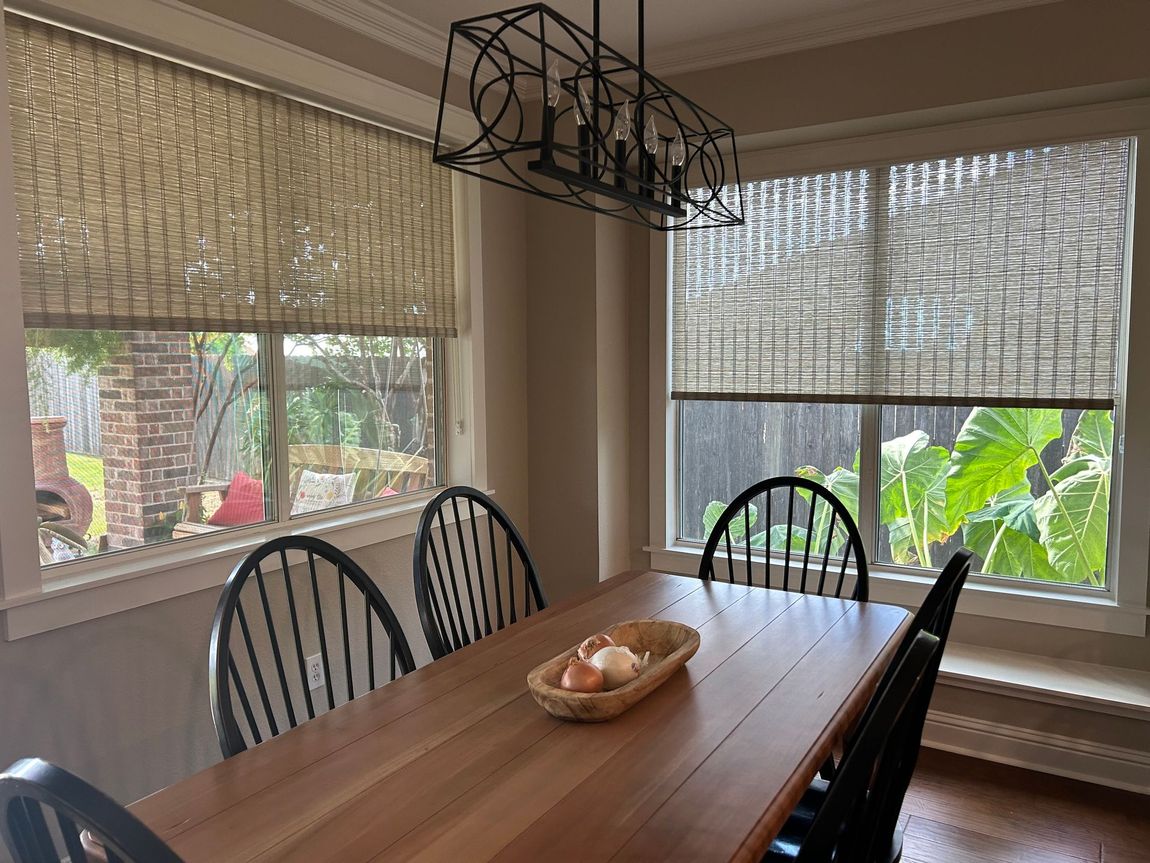 A living room with a table and chairs and a window with a roman shade.