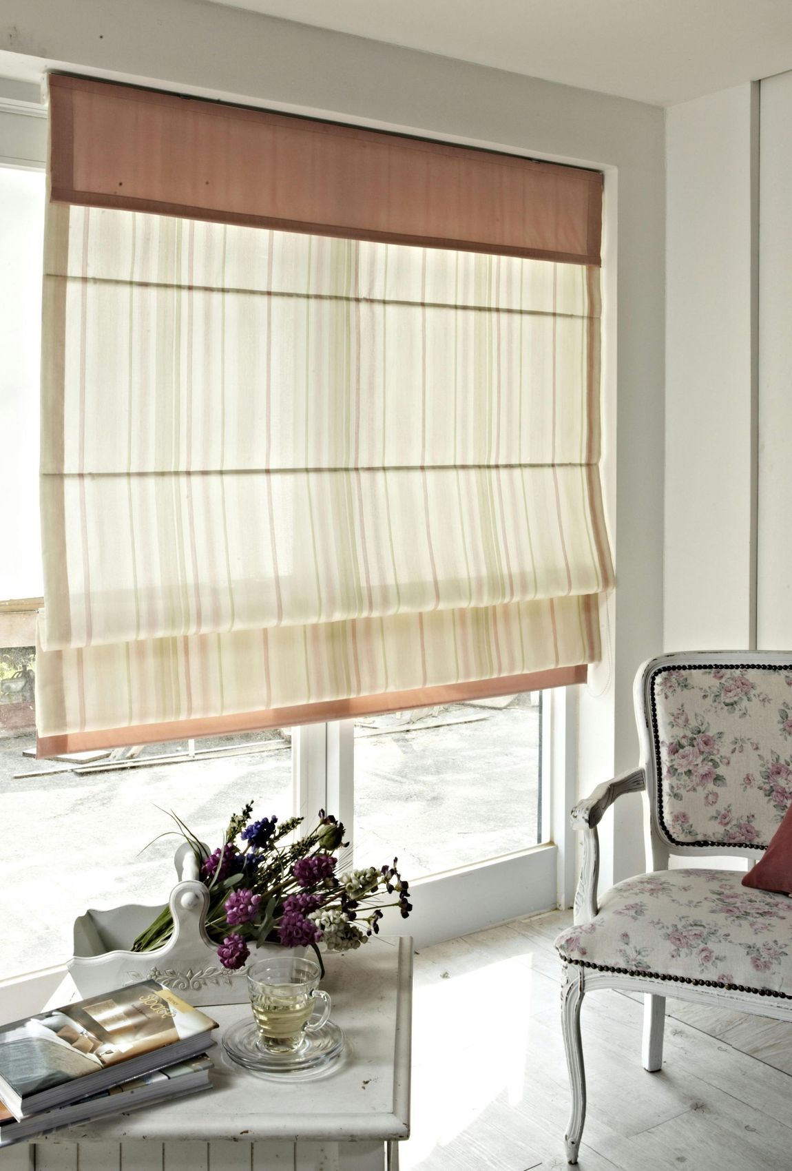 A living room with a table and chairs and a window with a roman shade.