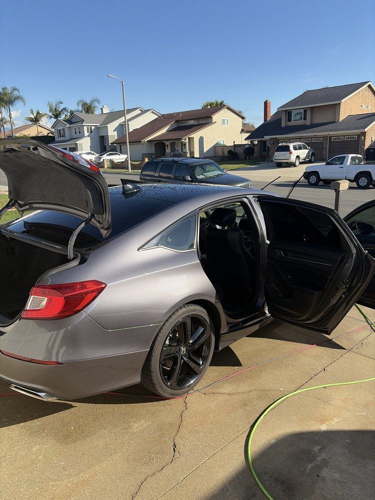 Gray car with open doors and trunk parked in a residential driveway on a sunny day.