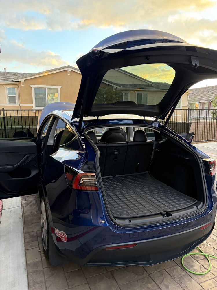 Blue Tesla Model Y with open trunk in a driveway.
