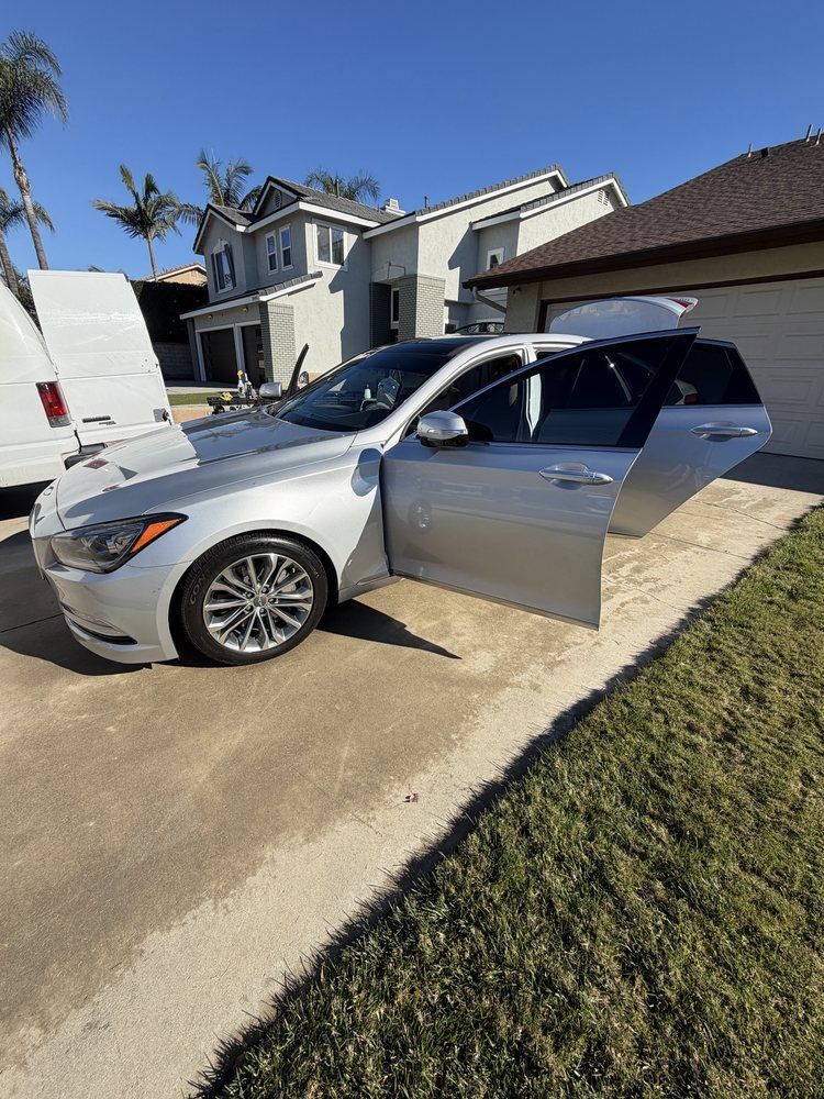 Silver car with open doors parked on driveway, grass, and houses in background.