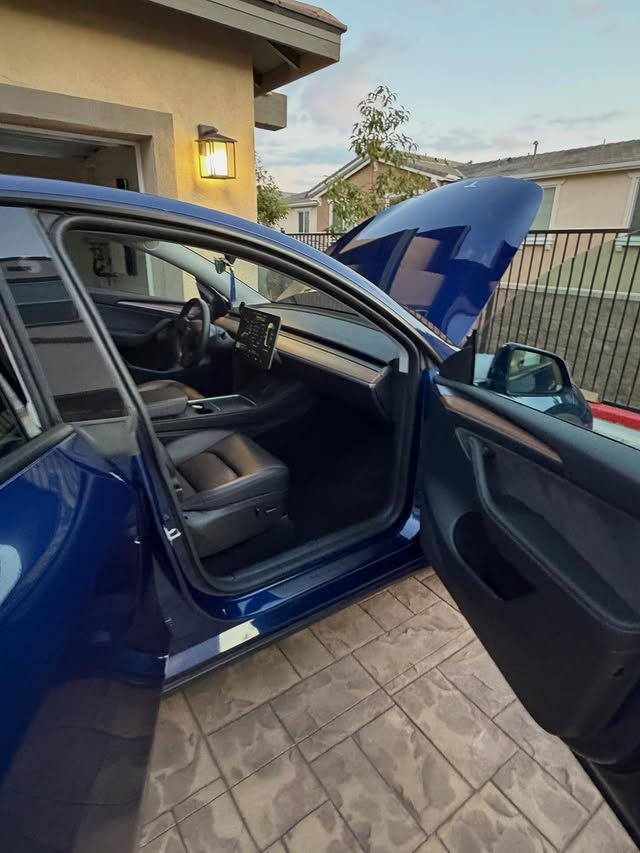 Blue Tesla car with the hood and door open, parked in front of a garage.