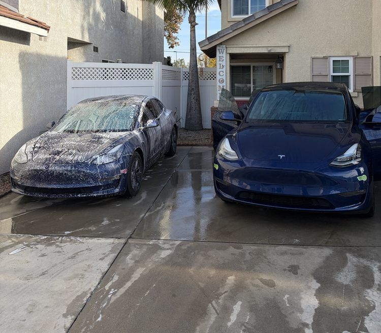 Two blue Tesla cars being washed in a driveway. One is covered in soap.