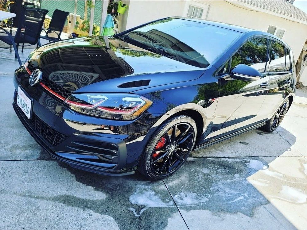 Black Volkswagen GTI parked on a concrete surface, red accents, sunny outdoor setting.