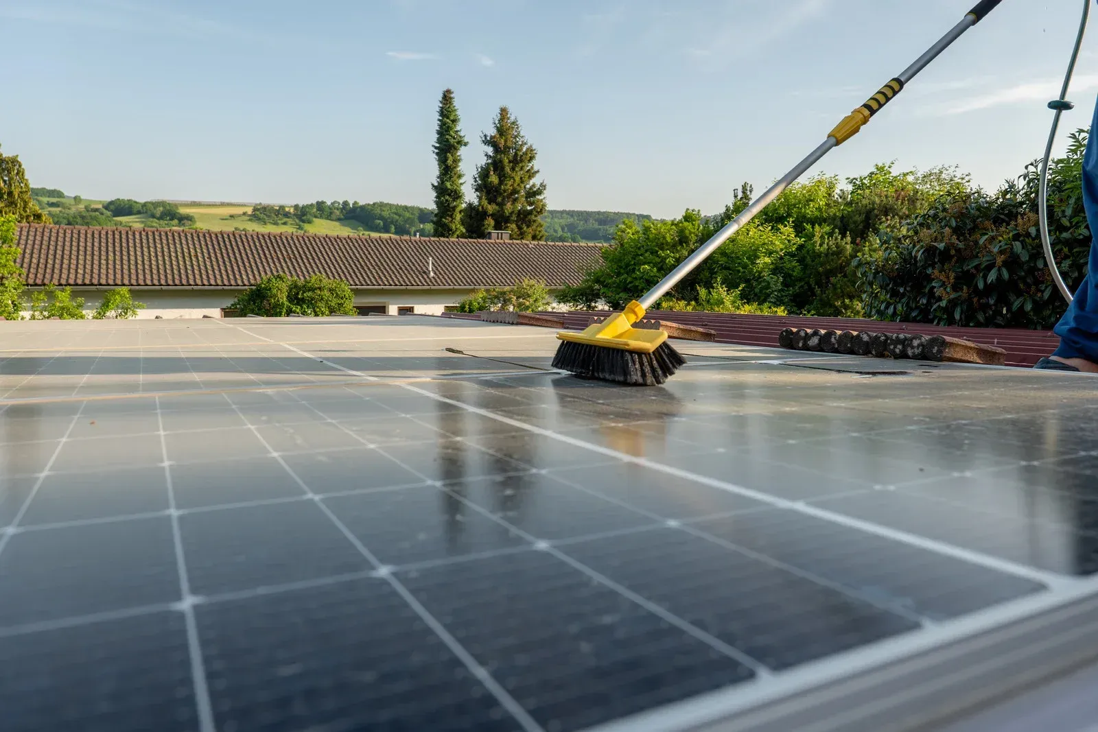 Solar panels being cleaned with a long-handled brush on a rooftop.