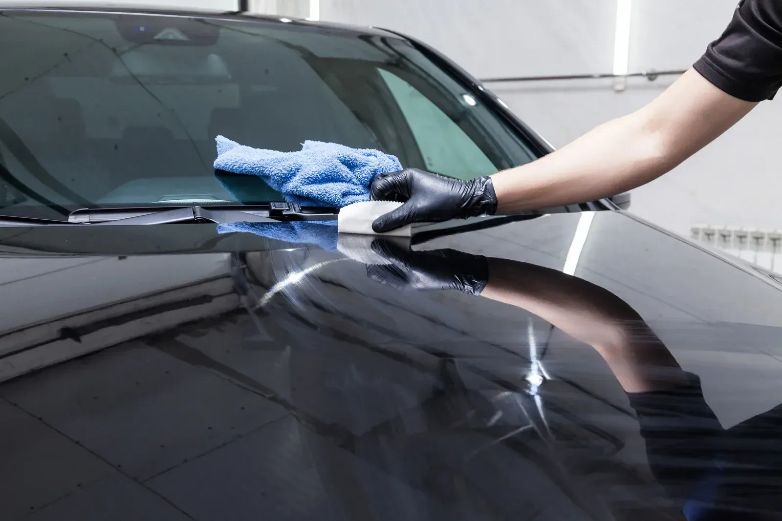 Person applying car wax to a black vehicle using a pad and microfiber cloth.