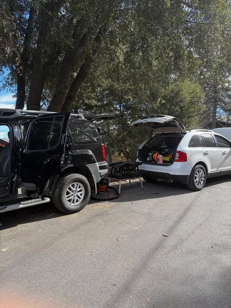 Black SUV and white station wagon parked on a road, both with open back hatches.