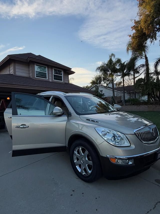 Tan Buick Enclave parked in a driveway with door open, house and blue sky in background.