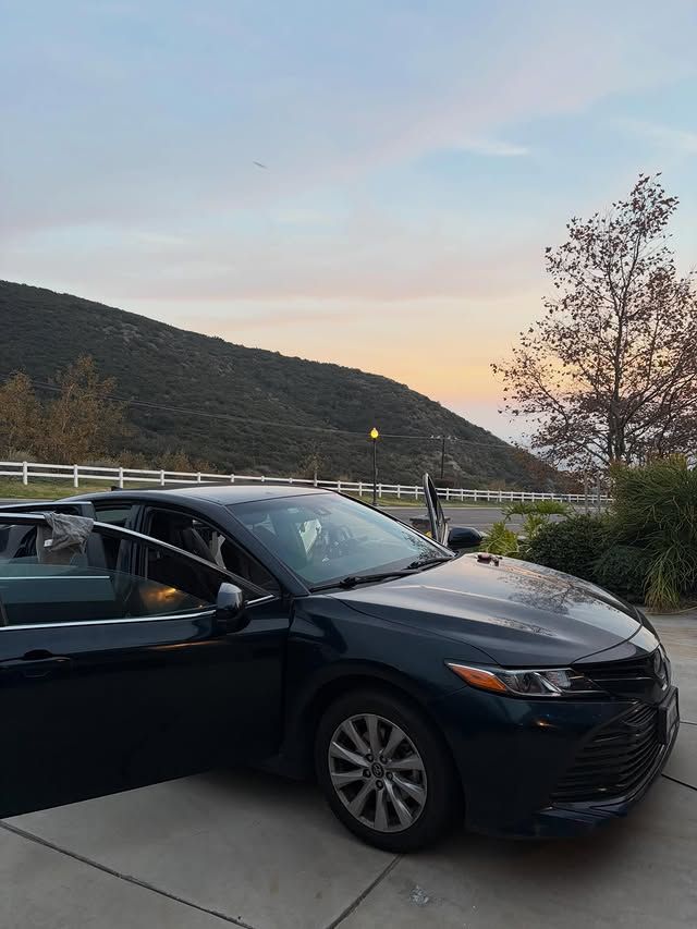 Dark green sedan with open doors parked near a mountain road at dusk.
