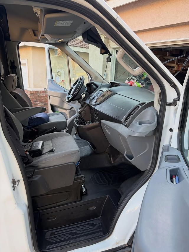 Interior of a white van, showing the driver's area with seats, dashboard, and open door.