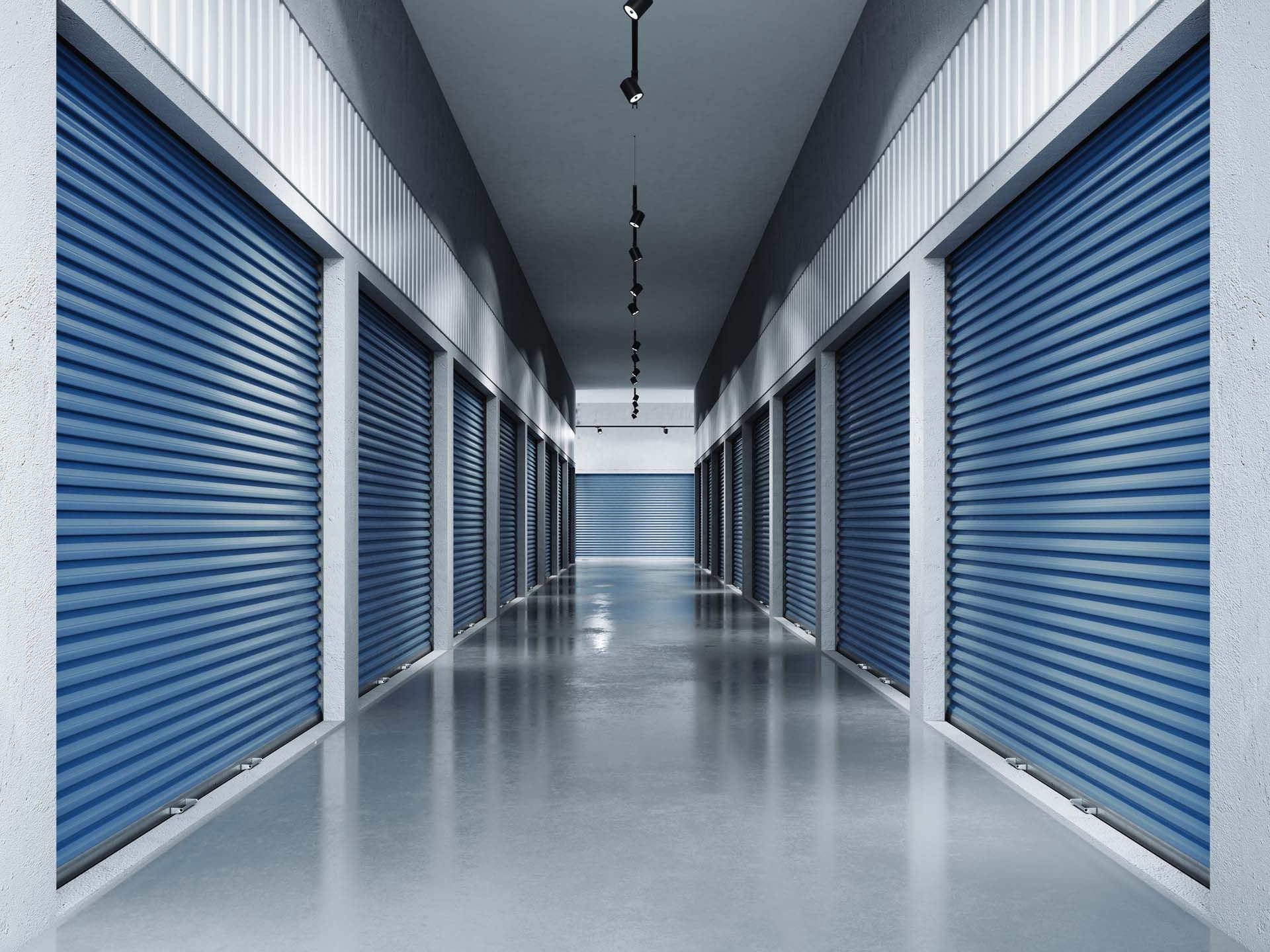 Clean hallway of indoor storage units featuring closed blue roll-up doors on both sides. Clean hallway of indoor storage units featuring closed blue roll-up doors on both sides.