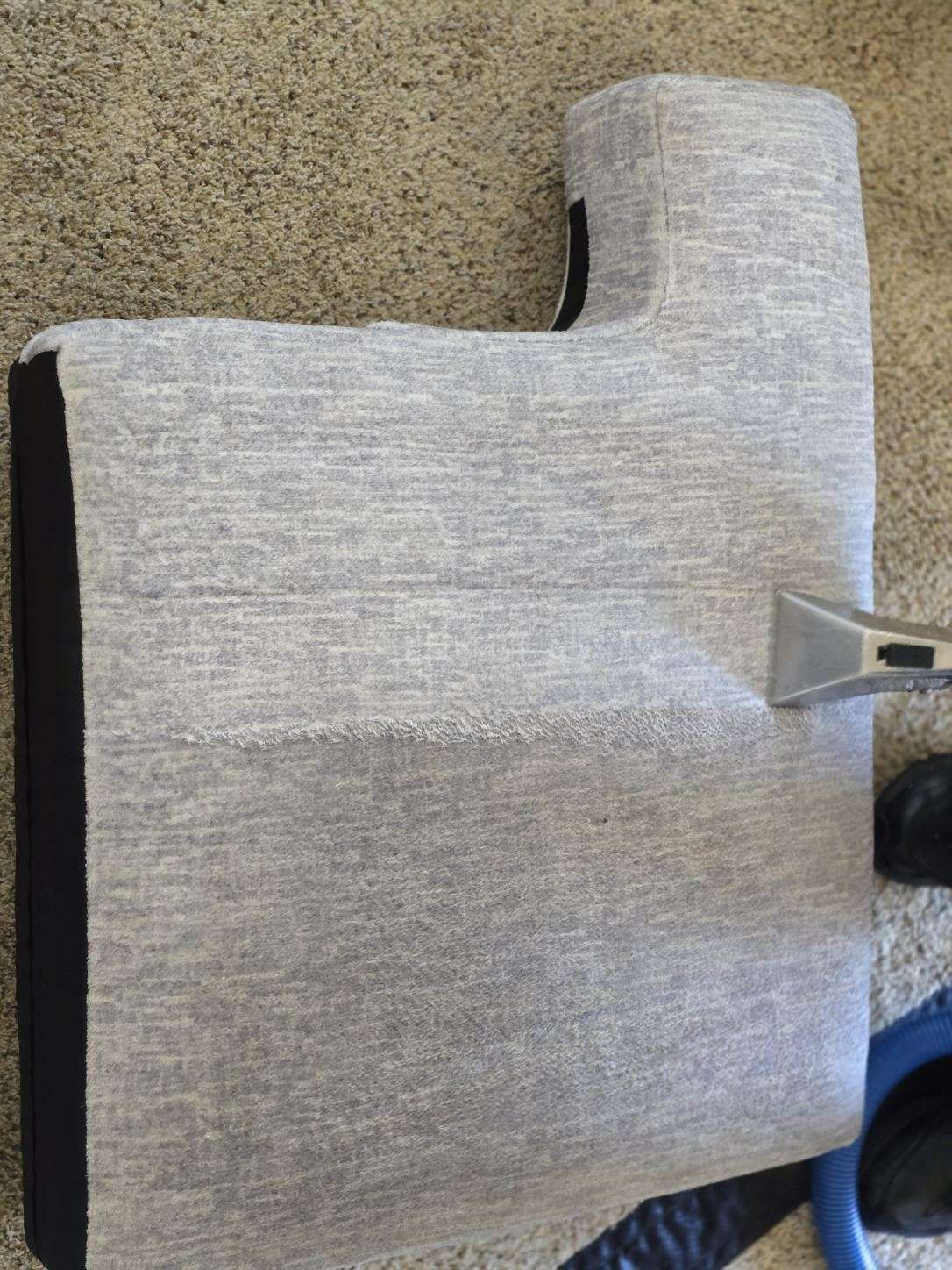 A grey fabric cover draped over a black, L-shaped object. A section of grey carpet is in the background.