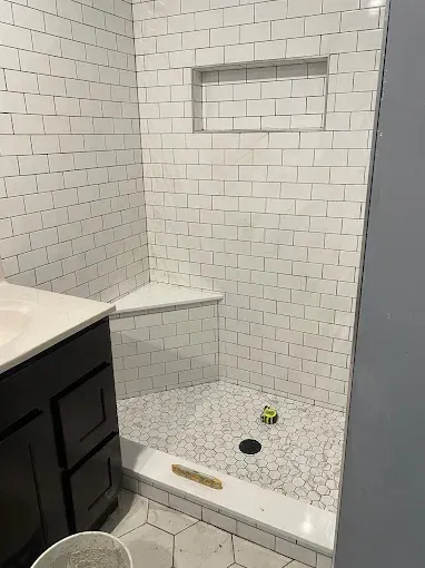 A bathroom shower with white subway tile walls, a built-in corner seat, a recessed niche, and white hexagon floor tiles.