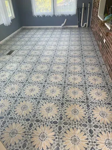 A room with patterned blue and beige vintage-style tiles on the floor, windows with white curtains, and a brick wall.