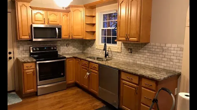A kitchen with oak cabinets, stainless steel appliances, granite countertops, and a white subway tile backsplash.