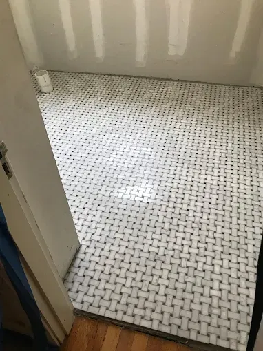 A room with white and gray woven-pattern mosaic marble floor tiles and unfinished drywall walls.