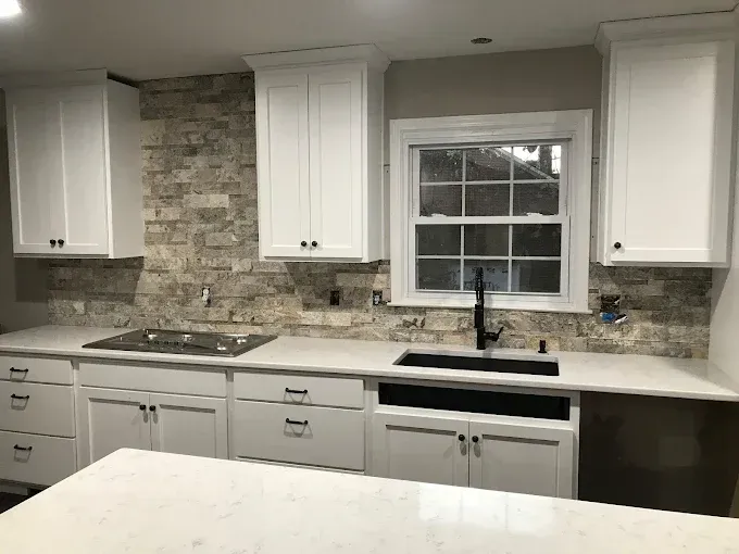 A kitchen featuring white cabinets, a stone backsplash, a white countertop, a black sink, and a black cooktop.