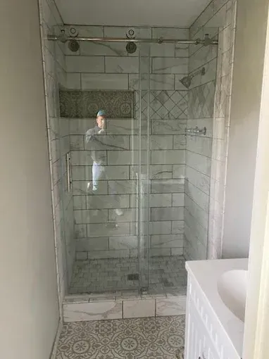A tiled walk-in shower with a glass sliding door and a built-in recessed shelf, featuring white subway-style wall tiles.