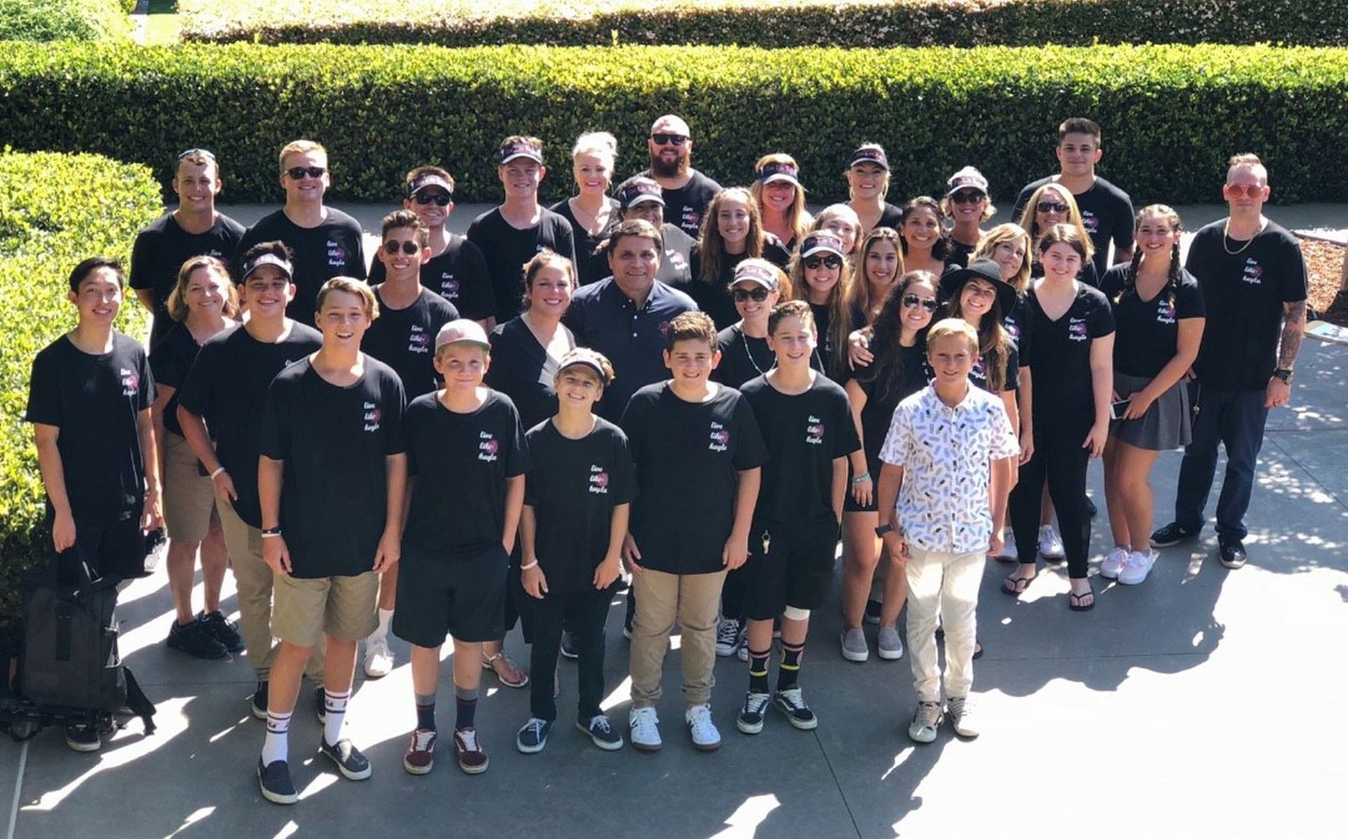 LLK  Team in black shirts and khaki shorts posing outside near greenery.