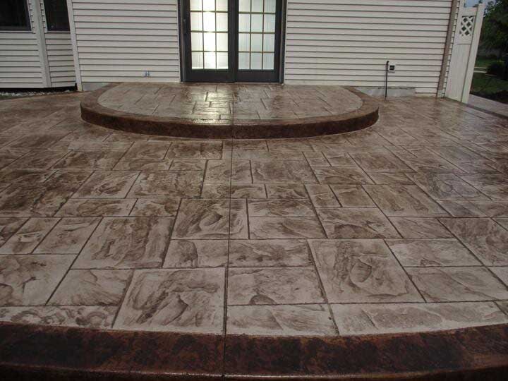 Stamped concrete patio with a dark brown border and steps leading to a door.