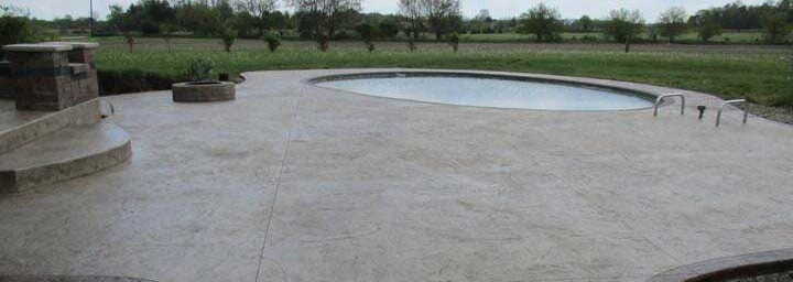 A concrete patio with a huge and round swimming pool in the background