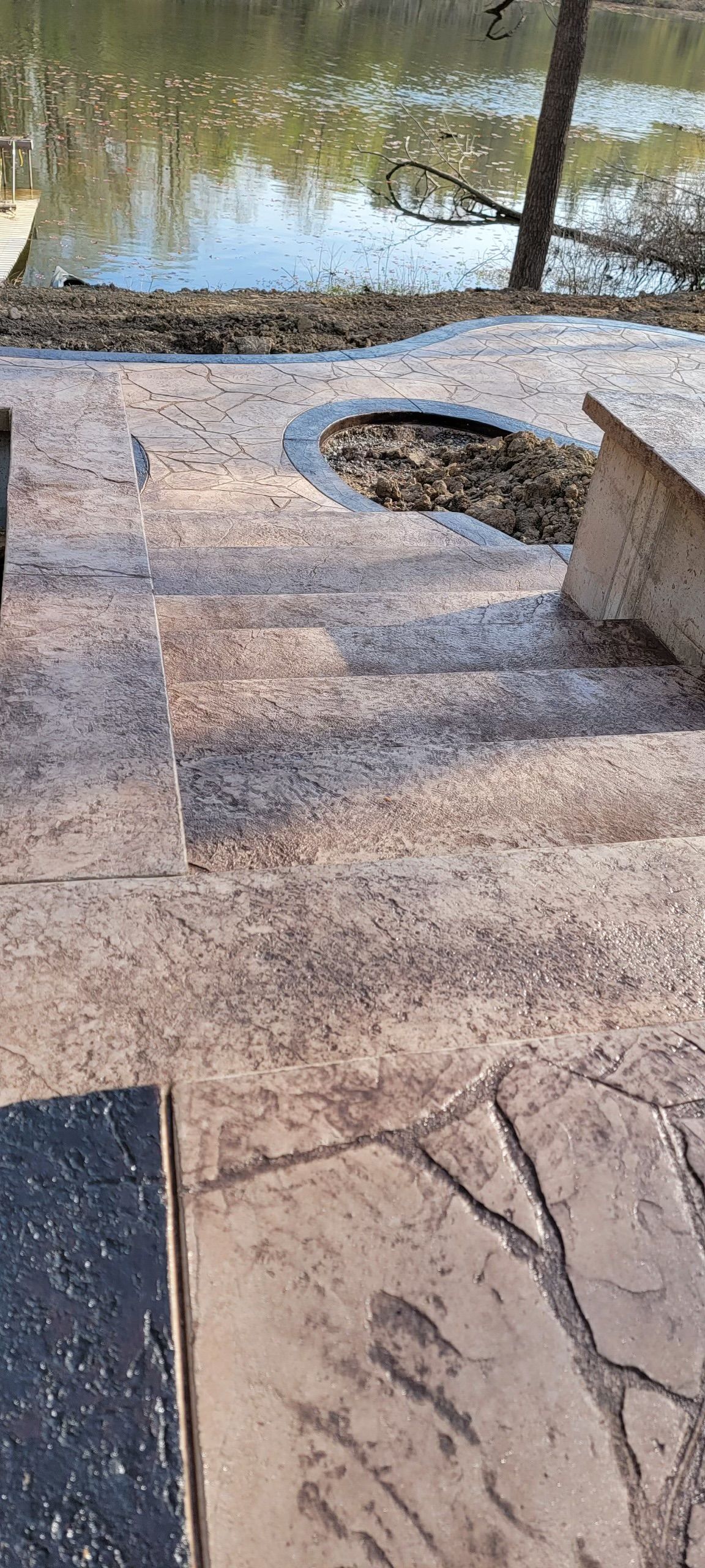 A concrete patio with a fire pit next to a lake