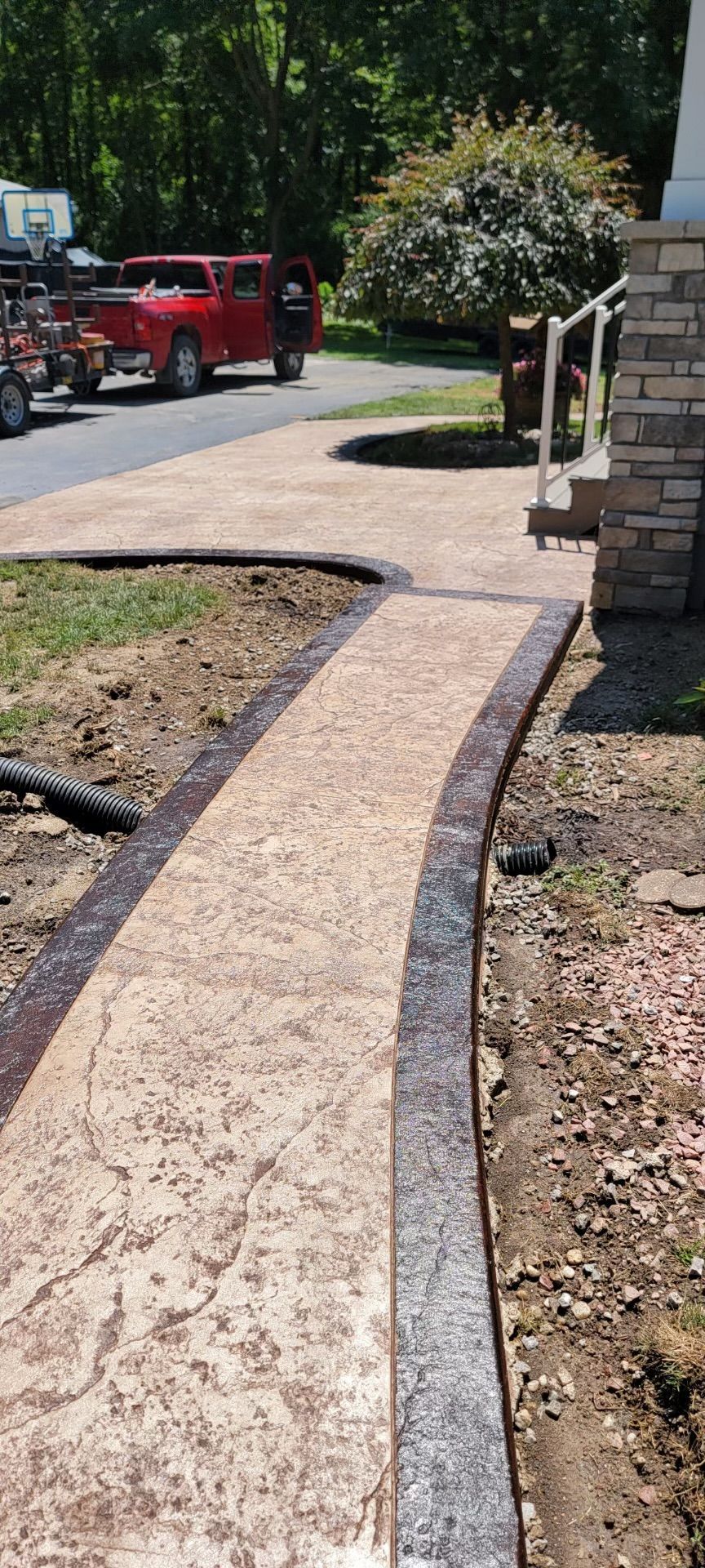 A red truck is parked on the side of the road next to a concrete walkway
