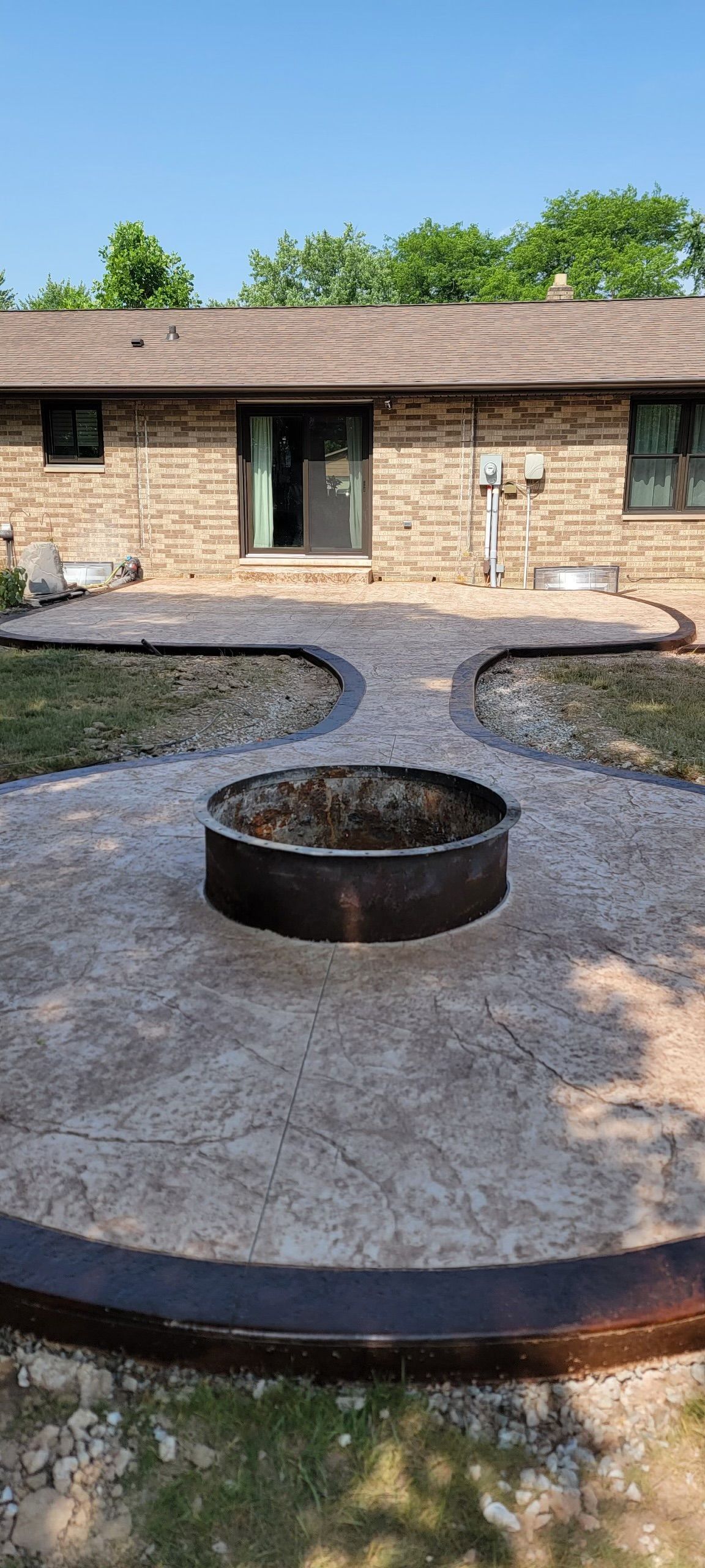 A fire pit is in the middle of a concrete patio in front of a brick house