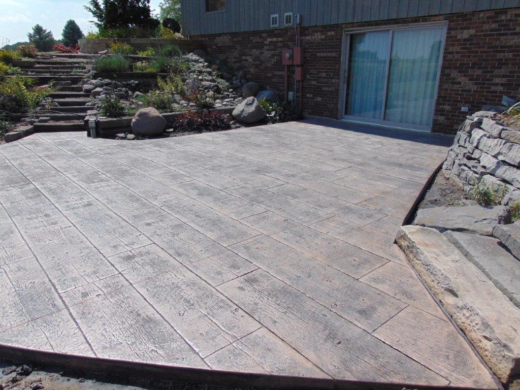 Concrete patio with stamped wood plank pattern. Steps lead up to a garden.