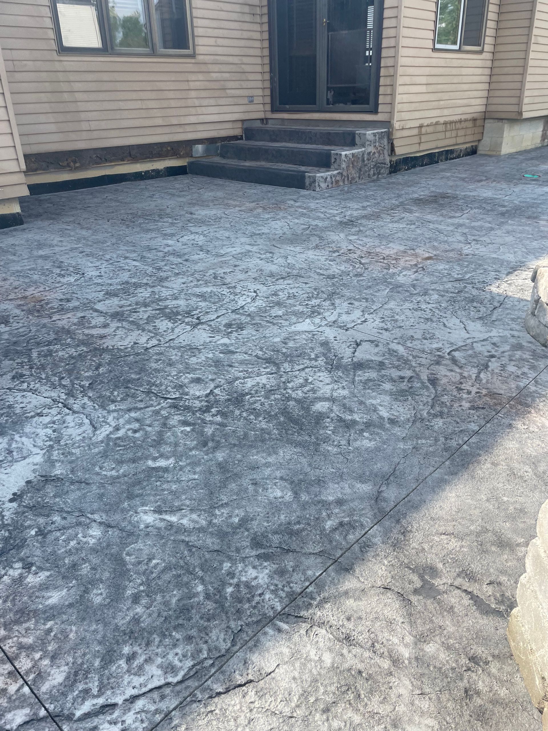 Stamped concrete patio leading to a house entrance with steps. Gray and white texture.