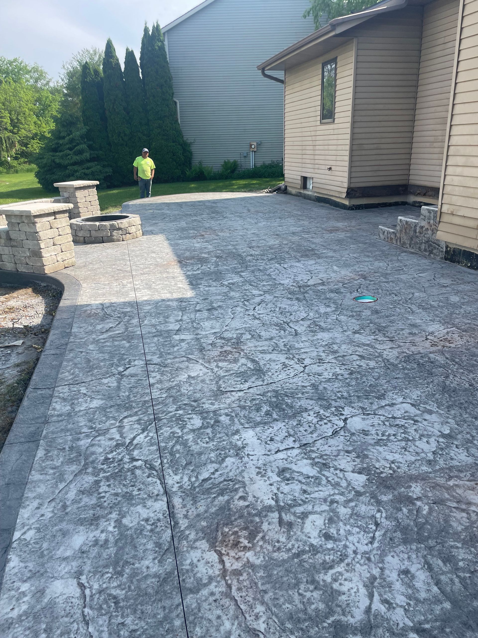 Newly installed gray stamped concrete patio next to a tan house and green lawn.