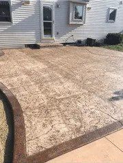 Stamped concrete patio with a dark brown border and tan coloring, next to a house.