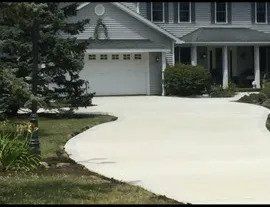 A light-colored concrete driveway curves toward a two-story gray house with a white garage door.