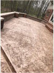 Stone textured patio with brick border, set against trees and a building's side.