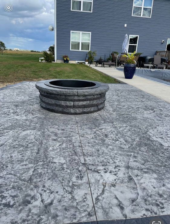 A fire pit is sitting on a concrete patio in front of a huge house