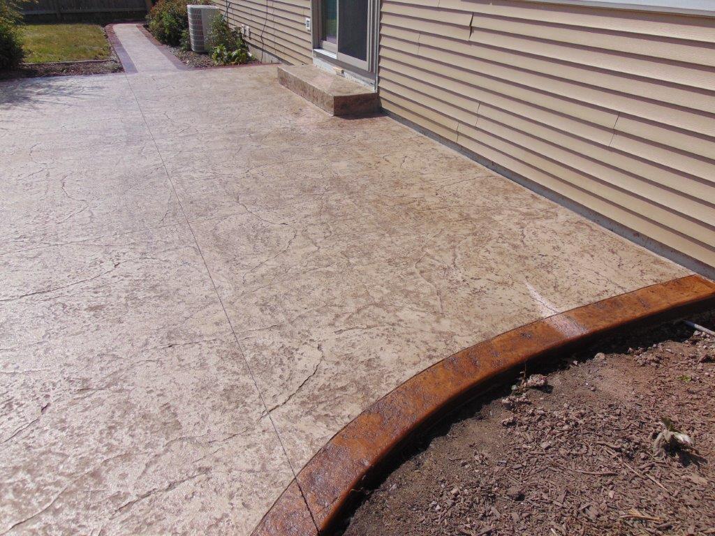 Stamped concrete patio with a dark border next to a beige house.
