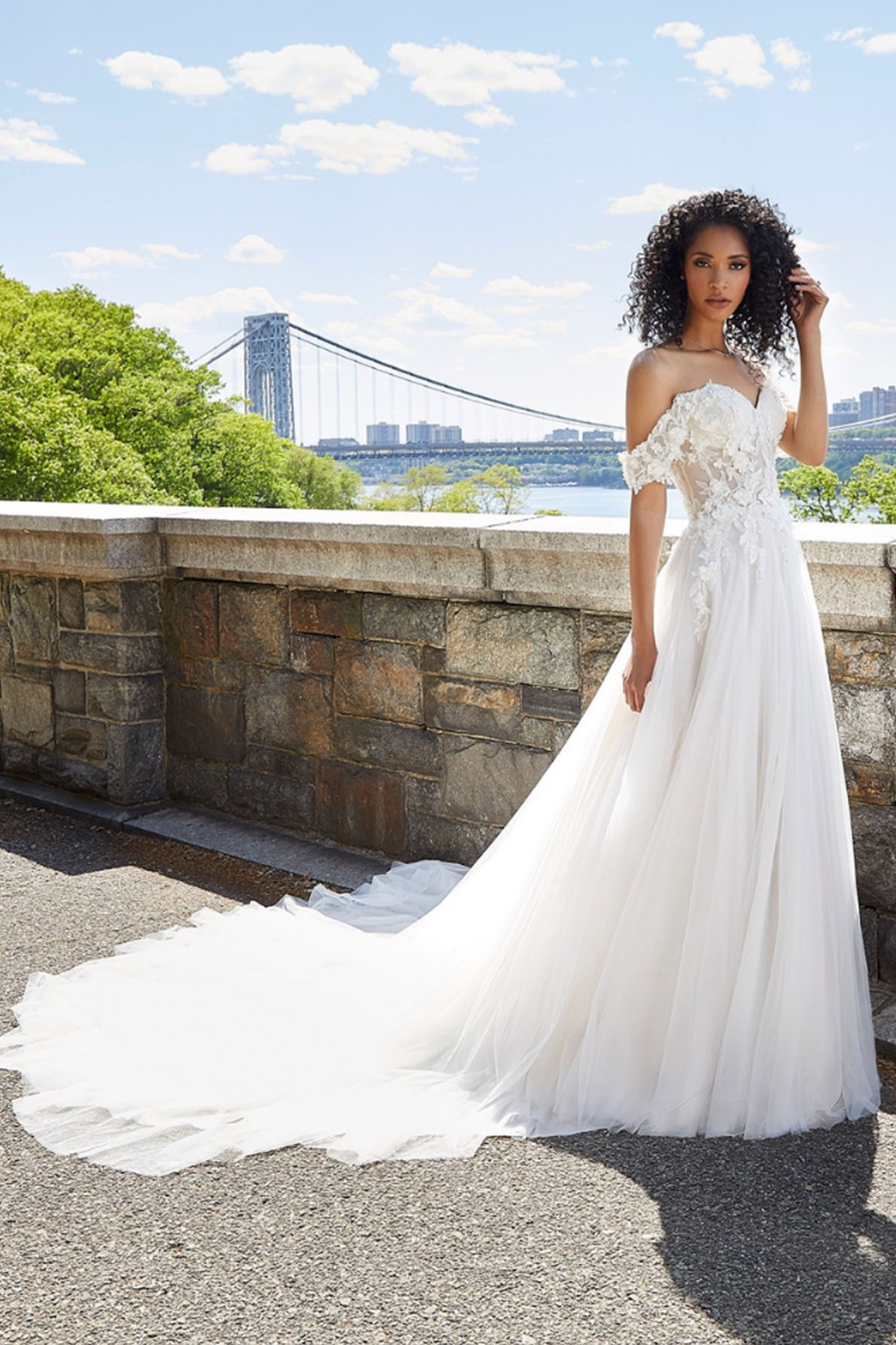 Una donna con un abito da sposa bianco è in piedi accanto a un muro di pietra.