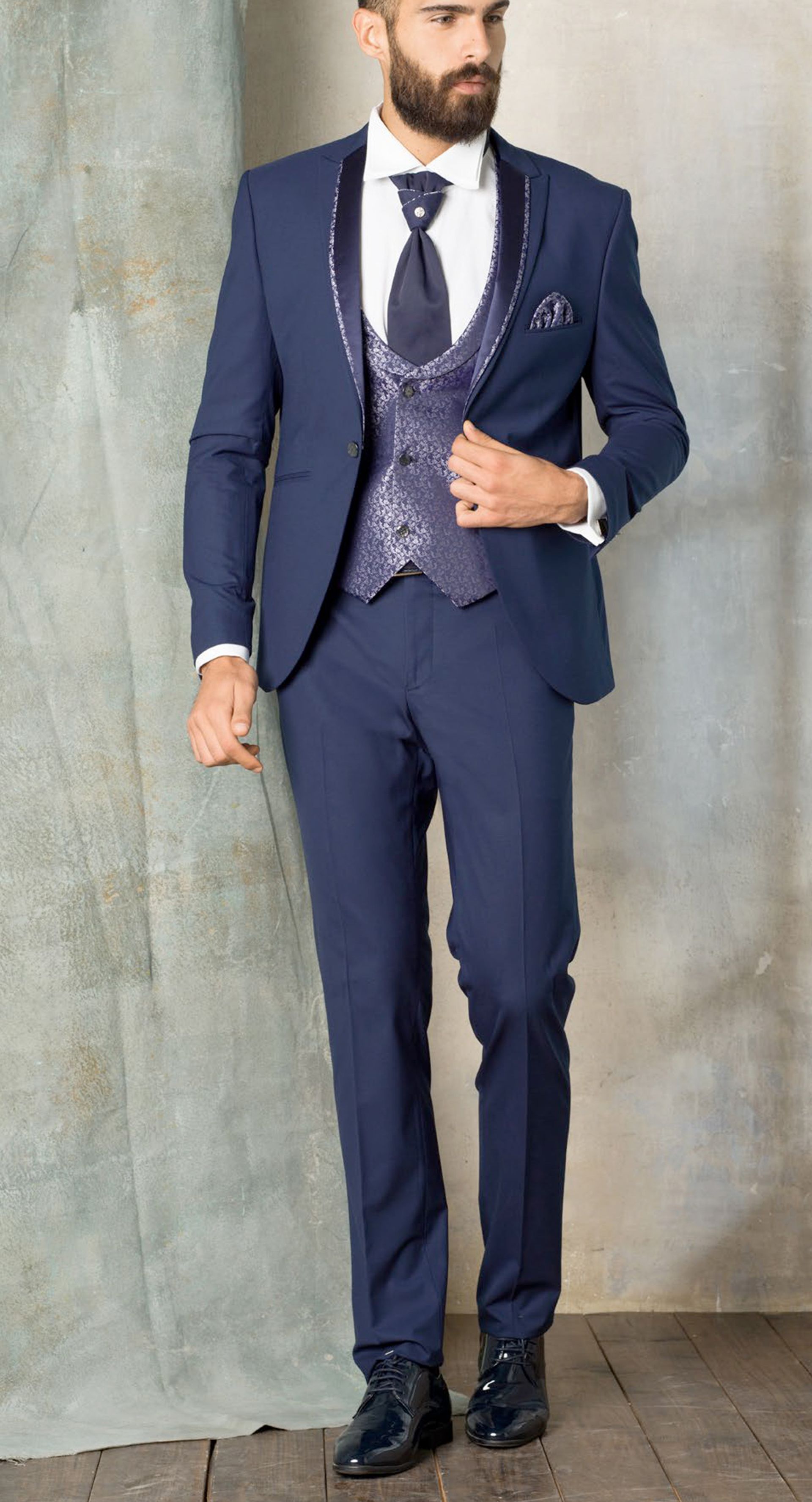 Un uomo con la barba indossa un abito blu e una cravatta.