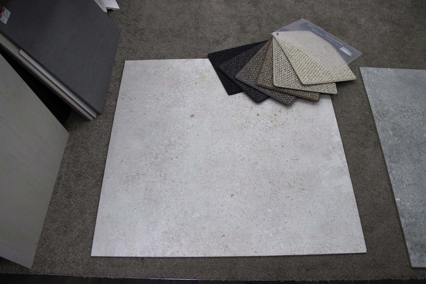 A Square Tile Is Sitting on A Carpet Next to A Stack of Tiles — Traditional Tiles & Flooring In Woree, QLD
