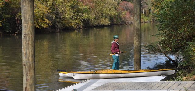 Person standing on a canoe by a calm river in a wooded area