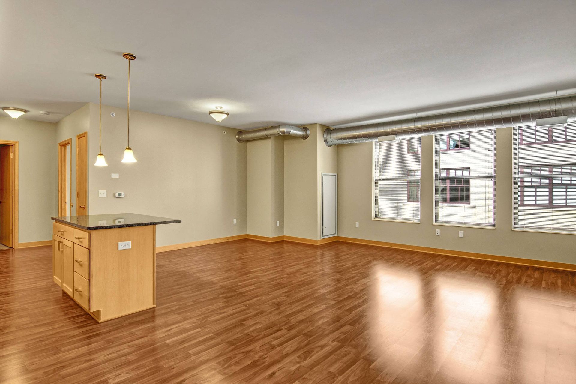 Open-concept living space with hardwood floors, kitchen island, large windows, and neutral walls.