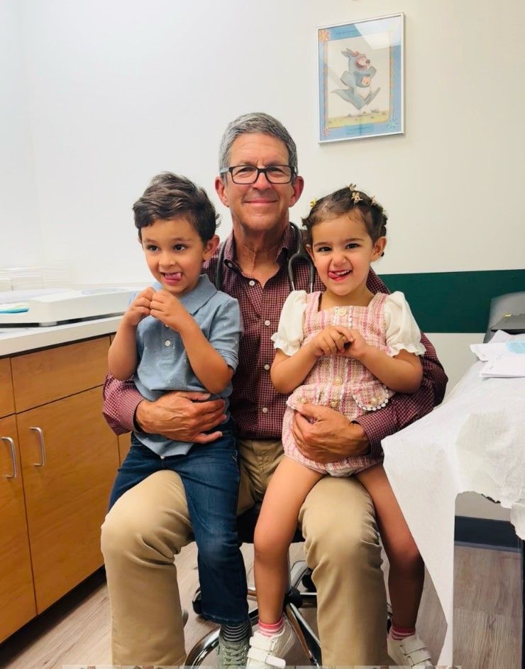 A man is sitting in a chair with two children on his lap.