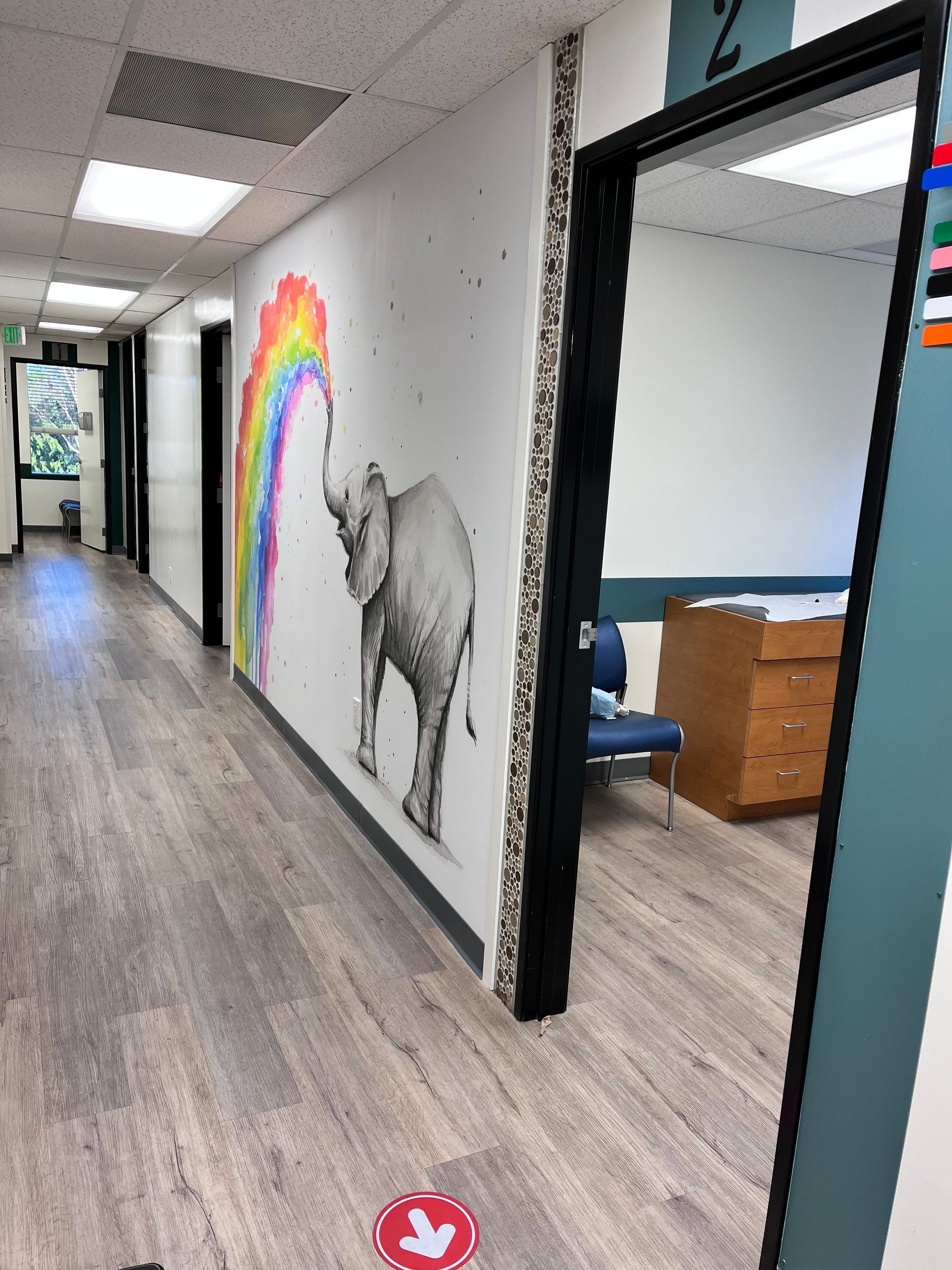 A hallway with a painting of an elephant and a rainbow on the wall.