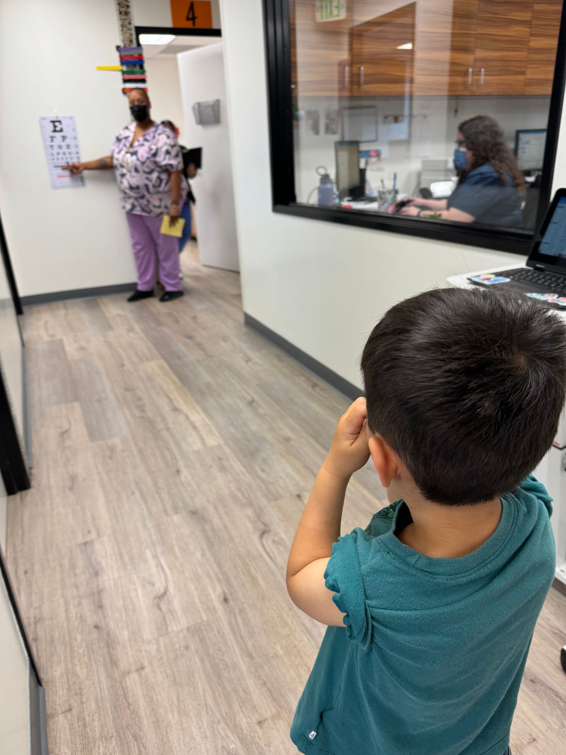 A young boy is standing in a hallway looking out a window.