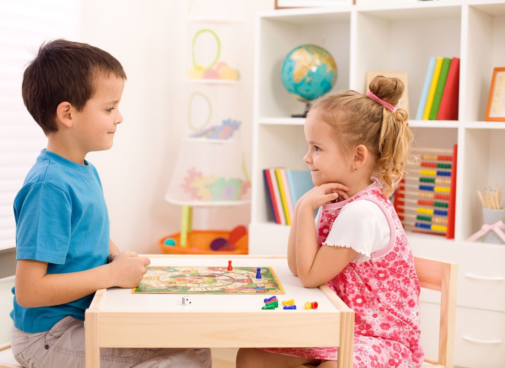 A boy and girl are sitting at a play table looking at each other