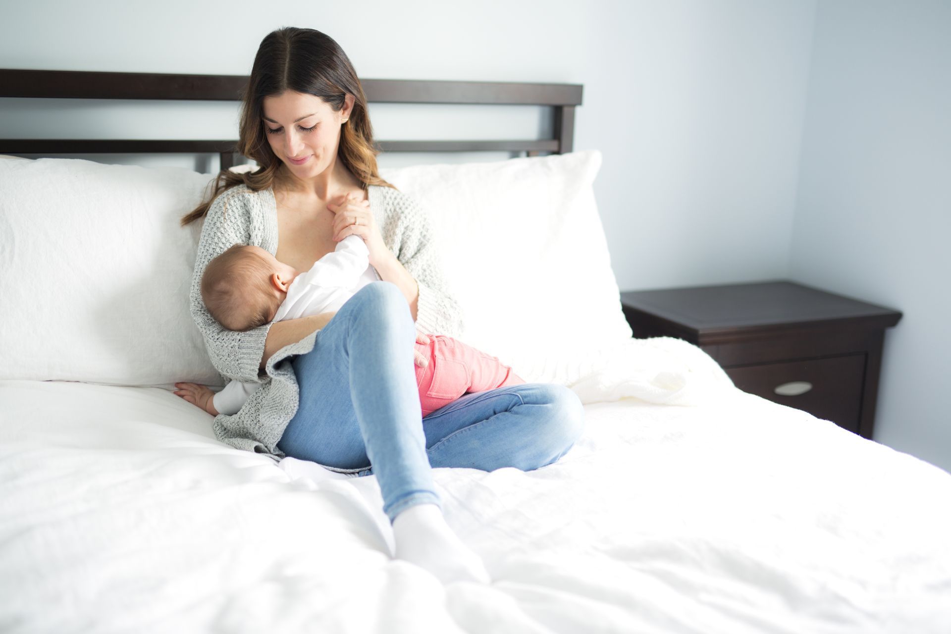 A woman is sitting on a bed breastfeeding her baby.