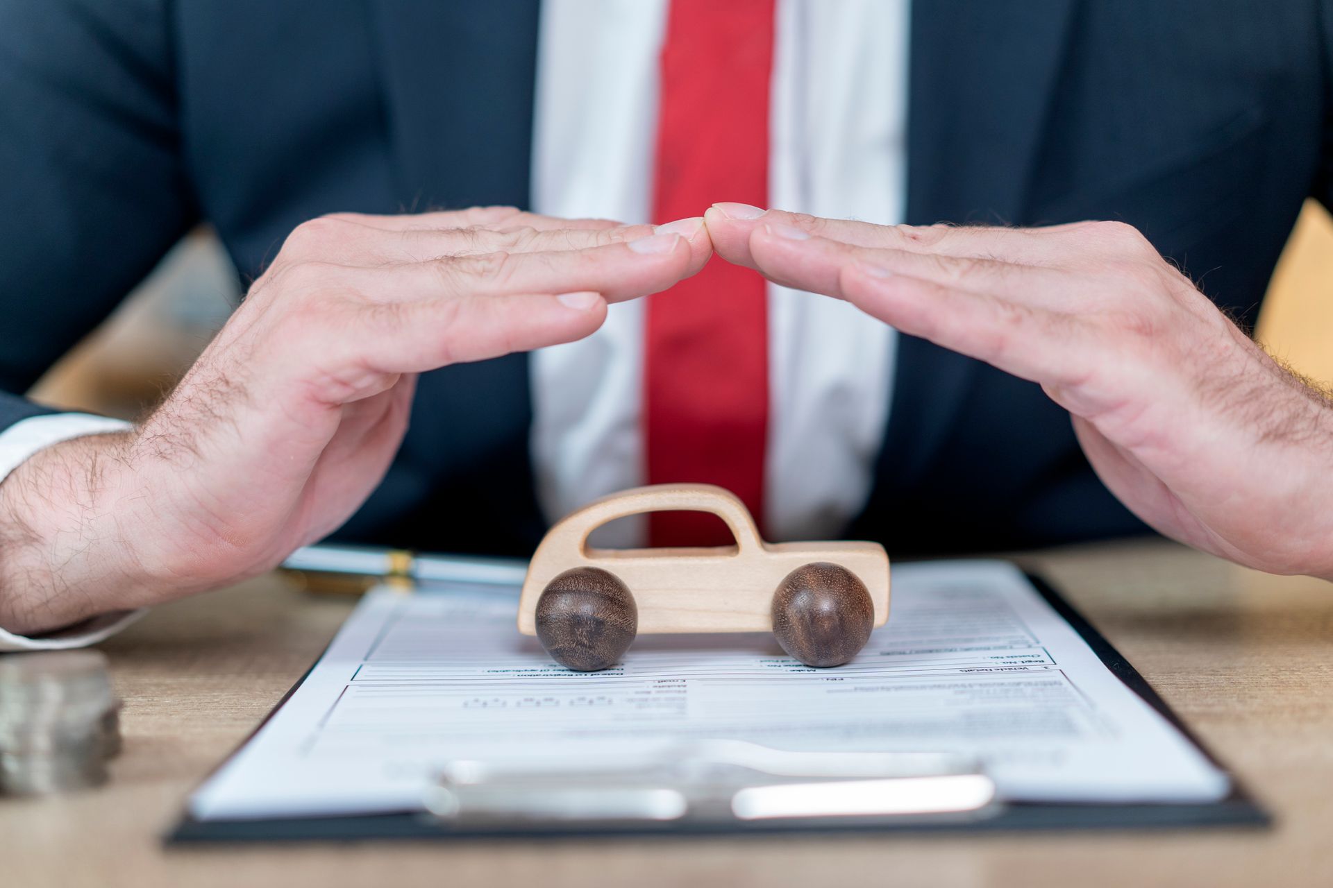 A businessman covering a toy car with his hands, symbolizing car insurance protection and care.