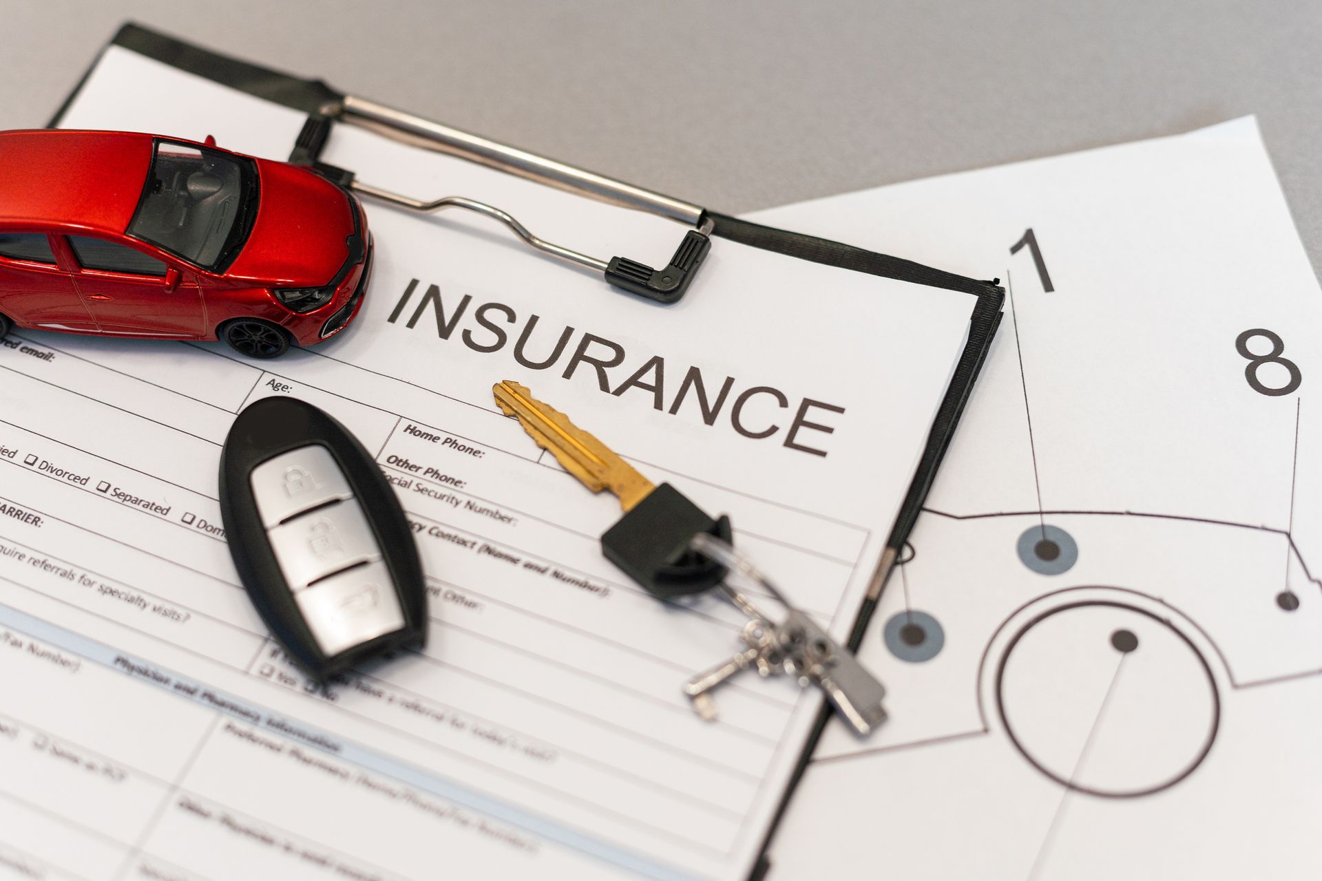 Top view of an auto insurance claim form, car key, and red toy car placed on a desk surface.