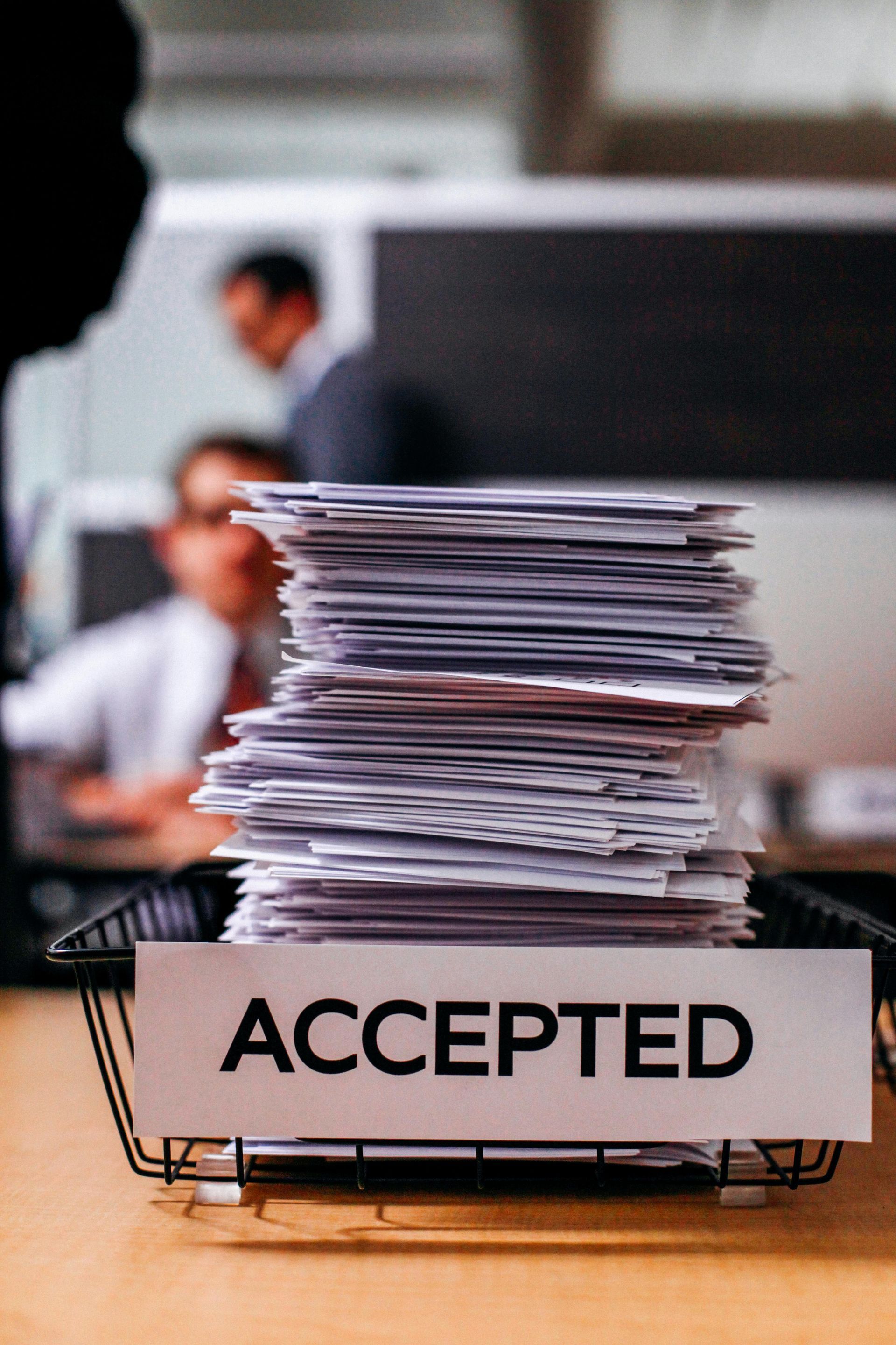 A stack of papers in a basket with a sign that says accepted