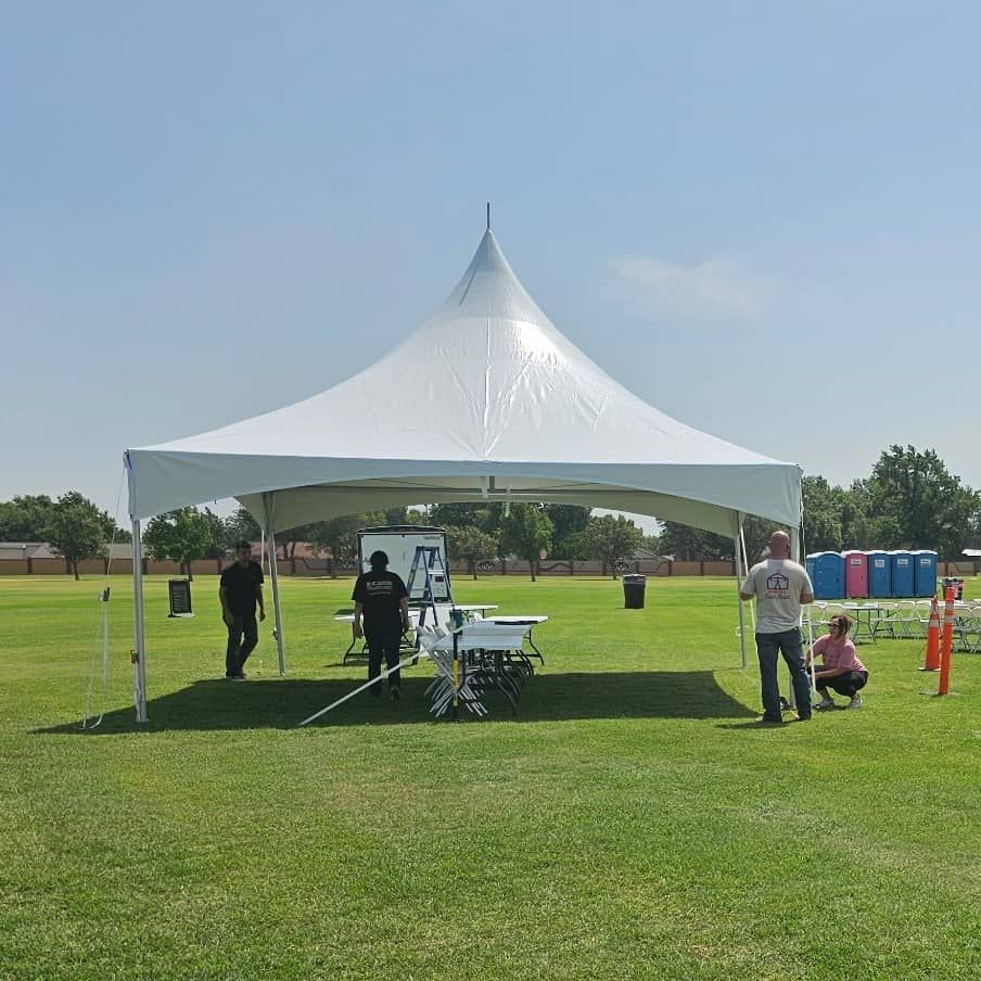 large white tent rental being set up by people on a grass field